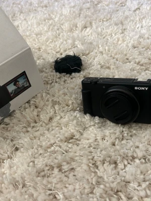 Sony svart digitalkamera med vridbar skärm - Snygg svart digitalkamera från Sony med kompakt design och vridbar LCD-skärm. Kameran har ett robust kamerahus i plast och metall, samt ett objektivskydd. Perfekt för vloggning och resor tack vare den smidiga storleken och smarta funktioner.