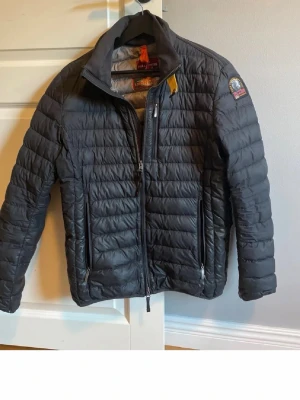 Svart dunjacka från Parajumpers - Snygg svart dunjacka från Parajumpers med quiltad design, hög krage och dragkedja framtill. Jackan har två sidofickor med dragkedja och en bröstficka. Märkets logga sitter på ärmen. Perfekt för kalla vinterdagar. priset är inte spikat.