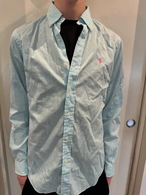 Randig skjorta från Polo Ralph Lauren - Snygg ljusblå och vit randig skjorta från Polo Ralph Lauren i storlek S. Modellen är 193 cm och väger 68 kg.
