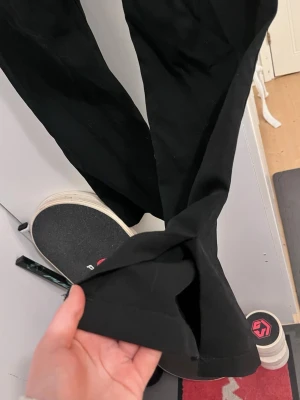 Svarta kostymbyxor bootcut - Säljer ett par svarta kostymbyxor med bootcut och pressveck. Byxorna har två bakfickor och hällor för skärp. Klassisk och stilren modell som passar till många olika looks. Byxorna har även slits längst ner.