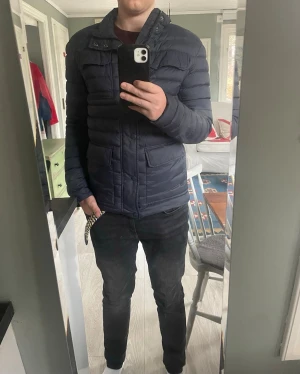 Marinblå dunjacka från Colmar - Snygg marinblå dunjacka från Colmar med quiltad design och hög krage. Jackan har flera praktiska fickor framtill, diskret logga på ärmen och stängs med både dragkedja och knappar. Perfekt för kalla vinterdagar och riktigt stilren look passar perfekt till en grich outfit nu i vår nypris 1800 mitt pris 900