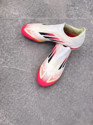 Addis f50 pro  - Ett par snygga vita fotbollsskor med rosa och gula detaljer. De är lite använda men fortfarande i bra skick och ser riktigt bra ut på planen. Perfekta för dig som vill ha både stil och prestanda 