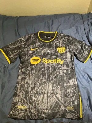 Barcelona matchtröja svart/gul Nike - Snygg FC Barcelona matchtröja i svart med gult tryck och detaljer. Tröjan har ett unikt grafiskt mönster, klubbmärke och Nike-logga på bröstet samt sponsortryck från Spotify. Tillverkad i lätt och ventilerande material, perfekt för fotboll eller träning.