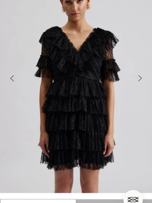 Svart volangklänning i spets - Supersnygg svart kortklänning med flera lager volanger och spetsdetaljer. Klänningen har v-ringning både fram och bak samt korta ärmar med volang. Perfekt för dig som vill sticka ut med en unik och trendig look. Använd en gång nypris 2800kr