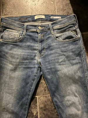 Blå Replay Hyperflex jeans - Snygga blå jeans från Replay med Hyperflex-teknologi som ger extra stretch och komfort. Klassisk femficksmodell med ljus tvätt och subtila slitningar. Märkesdetaljer på ficka och bak vid linningen. Perfekta för en avslappnad och trendig stil. Inga defekter, använts fåtal gånger. Kvitto finns 