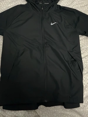 Nike miler S - Snygg svart hoodie från Nike running  med hel dragkedja framtill och klassisk vit Nike-logga på bröstet. Hoodien har huva och två sidofickor. Tillverkad i ett mjukt och bekvämt material som passar perfekt till en sportig stil.