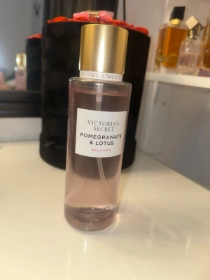 Victoria's Secret Pomegranate & Lotus mist - Fräsch body mist från Victoria's Secret med doft av granatäpple och lotus. Flaskan är cylinderformad i genomskinlig plast med ljusrosa vätska och har ett elegant guldfärgat lock. Perfekt för dig som gillar fruktiga och blommiga dofter.