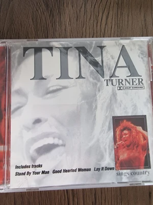 Tina Turner CD - Sings Country - CD-skiva med Tina Turner där hon sjunger countrylåtar. Omslaget är i plast med svartvit design och ett foto på Tina Turner med rött hår. Albumet innehåller låtar som 'Lay It Down', 'Stand By Your Man' och 'Soul Deep'. Perfekt för dig som gillar klassisk country och Tina Turner.