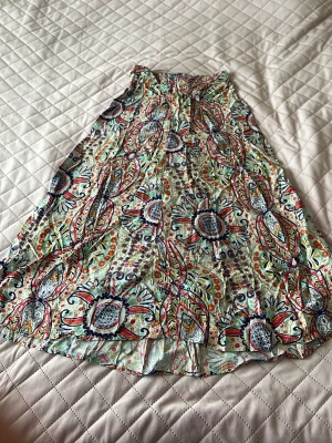 Mönstrad långkjol i bomull - Färgglad långkjol med blommigt och paisley-inspirerat mönster i blått, rött, orange och grönt. Kjolen har en lätt utsvängd form och är gjord i mjuk bomull, perfekt för varma dagar. Midjan är elastisk för extra komfort.