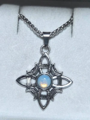 Halsband med silverfärgat månformat hänge - Unikt halsband med ett silverfärgat hänge i form av en stjärna och månar, dekorerat med en rund, skimrande opal-liknande pärla i mitten. Kedjan är grov och metallisk på 60 cm, och hänget har en fantasyinspirerad design som verkligen sticker ut, 3,5 x 3 cm. 