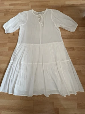 Som ny. Vit volangklänning med snörning - Luftig vit klänning med volanger och snörning vid halsen. Klänningen har halvlånga ärmar och en avslappnad passform. Perfekt för varma dagar och enkel att styla med accessoarer. Som ny, hade på mig en gång. Stort i storleken och pssssr S, M, L.