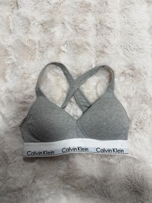 Grå sport-bh från Calvin Klein - Säljer en grå sport-bh från Calvin Klein med korsade axelband i ryggen och bred resår med logga. Bh:n är mjuk och utan bygel, tillverkad i stretchigt bomullsmaterial för extra komfort. Perfekt för dig som gillar enkel och stilren design. Pris kan diskuteras 💓