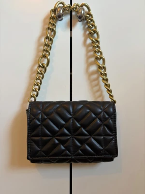 Svart  handväska med guldfärgad kedja - Snygg svart handväska från Zara med bred guldfärgad kedja som axelrem. Använd ett par gånger, i fint skick