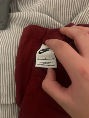 Vinröd Nike t-shirt i bomull - Säljer en vinröd t-shirt från Nike med klassisk vit logga broderad på bröstet. T-shirten har rund hals och är tillverkad i mjuk bomull, perfekt för en avslappnad och sportig stil.