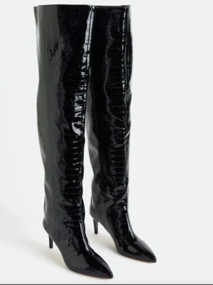 Svarta overknee stövlar med krokopräglad yta som nya! - H&M stövlar för dam i storlek 38. Höga stövlar i svart, glansigt material med krokodilpräglad yta och smal klack. Spetsig tå och slank siluett. Passar som vardags- eller feststövlar beroende på styling. Såå snygga!