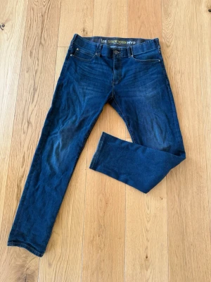 Mörkblå slim jeans från Lee - Säljer ett par mörkblå slim fit jeans från Lee Extreme Motion MVP. Jeansen har klassisk femficksdesign, stretchigt material och normal midja. Snygga slitningar framtill och Lee-logga på bakfickan. Perfekta för en avslappnad och trendig look.
