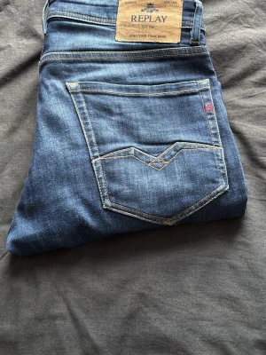 Blå jeans från Replay - Snygga blå jeans från Replay med klassisk femficksmodell och kontrastsömmar. Jeansen har en rak passform och är tillverkade i mjukt denimtyg. Bakfickan har en unik detaljsöm och Replay-lapp i midjan. Perfekta för en avslappnad och trendig look.