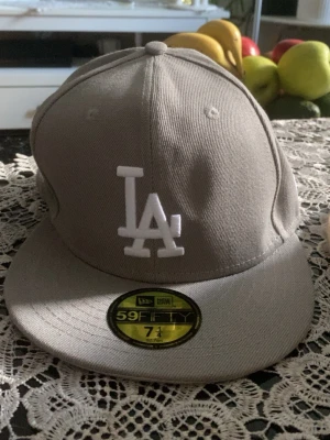 Grå LA Dodgers keps från New Era - Snygg grå keps från New Era med LA Dodgers-logga i vitt framtill och broderad 1988 World Series-märke på sidan. Modellen är 59FIFTY med platt skärm och klassisk passform. Perfekt för dig som gillar sport och streetstyle.