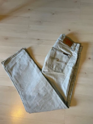 Ljusblå raka jeans från Nudie - Säljer ett par ljusblå jeans från nudie med rak passform och klassisk femficksdesign. Jeansen har en snygg vintagekänsla och är tillverkade i kraftigt bomullstyg. Perfekta för dig som gillar en avslappnad och tidlös stil. W 29 L 30
