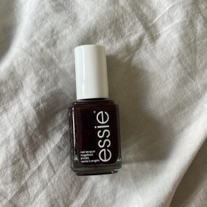 Mörkrött nagellack från Essie - Snyggt mörkrött nagellack från Essie med klassisk fyrkantig glasflaska och vit kork. Färgen är djup och elegant, perfekt för dig som gillar mörka toner på naglarna. Lacket har en krämig formula som ger ett jämnt och täckande resultat. Fått den som present och är ny och oöppnad 