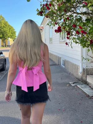 Rosa topp med rosett - Supersöt rosa linnetopp med breda axelband och stor rosett i ryggen. Toppen har en figurnära passform och är perfekt för varma dagar. Har sytt in banden men det går enkelt att sprätta upp eftersom jag inte klippt något i dem, använd en gång så som ny! Kom med prisförslag!