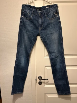Replay anbass - Säljer ett par klassiska blå jeans från Replay med raka ben och fem fickor. Jeansen har snygga slitningar och kontrastsömmar, samt Replay-logga på bakfickan. Perfekta för en avslappnad och trendig stil.