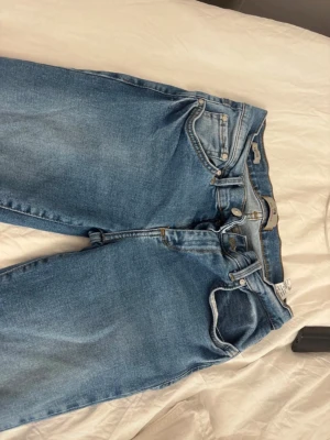 Blå raka jeans från Gina Tricot - Säljer ett par klassiska blå jeans från Gina Tricot med rak passform och normal midja. Jeansen har fem fickor, bälteshällor och stängs med dragkedja och knapp. Perfekta till vardags och lätta att matcha med olika stilar.