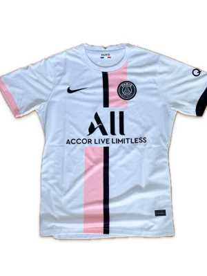 PSG 2021/2022 bortatröja Mbappé #7 - Snygg PSG matchtröja i vitt med rosa och svarta detaljer. Framsidan har PSG-logga, Nike-logga och sponsortryck, medan baksidan har Mbappé och nummer 7. Bättre pris vid snabb affär!