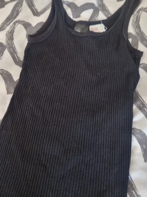 Ribbat svart set - Säljer ett svart ribbat set med linne och matchande shorts. Setet är tillverkat i mjukt, stretchigt tyg och har en enkel, stilren design med breda axelband på linnet. Perfekt för en avslappnad look. Inga defekter, men har legat I förrådet så något dammiga