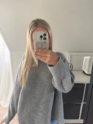 Grå stickad tröja från strandivarius - Mysig grå stickad tröja från strandivarius i en oversized modell. Tröjan har rund halsringning, långa ärmar och breda ribbade muddar vid ärmslut och nederkant. Perfekt för lager på lager och enkel att matcha med jeans eller kjol.
