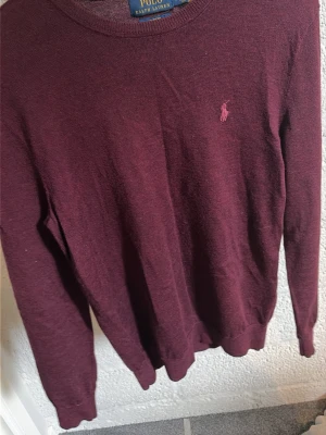 Vinröd merinoullströja Polo Ralph Lauren - Snygg vinröd stickad tröja från Polo Ralph Lauren i slim fit-modell. Tillverkad i tvättbar merinoull och har den klassiska broderade loggan på bröstet. Skriv om ni har några frågor!!