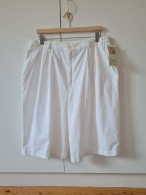 Vita vintage bermudashorts från City Look strl 48 - Säljer ett par vita bermudashorts från City Look med elastisk midja och knappstängning. Shortsen har raka ben, sidofickor och är tillverkade i ett lätt tyg som passar perfekt till sommaren. Storlek 48. Aldrig använd med prislapp och etikett. Material 100% bomull. Total längd 68 cm. Finns några gula fläckar som går att tvätta bort.