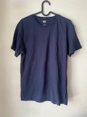 Mörkblå t-shirt från 157 - En basic mörkblå t-shirt från 157 i 100% bomull. Klassisk rund halsringning och korta ärmar. Perfekt för dig som gillar enkel och stilren design. Passformen är normal och materialet känns mjukt mot huden.