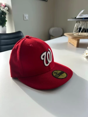 Röd New Era keps - Snygg röd keps från New Era, modell 59FIFTY, med broderad vit och svart 'W' framtill. Klassisk flat brim och strukturerad passform. Perfekt för dig som gillar streetwear och sportig stil.