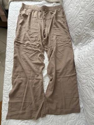 Beiga linnebyxor från H&M - Säljer ett par beiga linnebyxor från H&M med avslappnad passform och resår i midjan. Byxorna har raka ben och sidofickor, perfekta för en chill och stilren look. Materialet är lätt och luftigt, vilket gör dem sköna att bära under varma dagar.