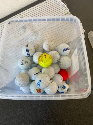 Plastlåda med blandade golfbollar köp en för priset skriv först - Säljer en transparent plastlåda fylld med olika golfbollar. De flesta är vita med tryck och logotyper, men det finns även en gul och en röd boll. Perfekt för dig som vill ha extra bollar till golfbanan eller träning.