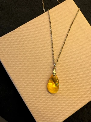Swarovski light topaz - Snyggt halsband med tunn guldfärgad kedja och en stor, droppformad gul kristall som hänge. Hänget har en facettslipad yta som reflekterar ljuset och ger ett riktigt coolt intryck. Perfekt för dig som vill sticka ut med en färgglad accessoar.
