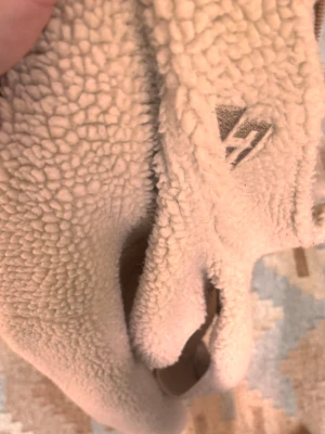 Beige teddyväst från Kari Traa - Mysig beige teddyväst från Kari Traa med två dragkedjeförsedda fickor och broderad logga på bröstet. Västen är tillverkad i fluffigt fleece-material och har en avslappnad passform. Perfekt för lager-på-lager och chill dagar.