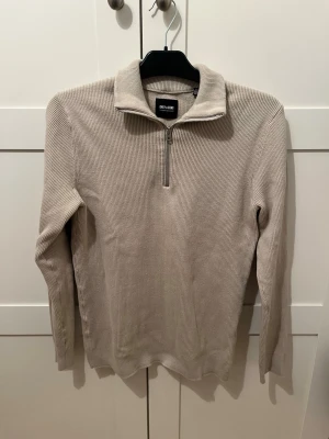 Beige tröja Only & Sons - Snygg beige ribbad tröja från Only & Sons med halv dragkedja och hög krage. Tröjan har lång ärm och är tillverkad i ett mjukt, stretchigt material som passar perfekt till lager på lager. Enkel och stilren design som funkar till det mesta.