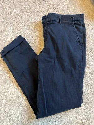 Mörkblå chinos från Mason’s - Snygga mörkblå chinos ifrån Mason’s. Byxorna har en enkel knappstängning i midjan och är tillverkade i ett mjukt bomullsmaterial. Perfekta för en stilren och avslappnad look.