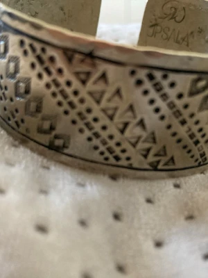 Brett silver armband - Säljer ett brett armband i silver från Uppsala hantverk med coola geometriska mönster av trianglar och rutor. Armbandet har en hamrad yta och är öppet så det är lätt att ta på och av. Perfekt för dig som gillar unika accessoarer med etno-vibe.