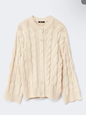 Beige kofta från Gina tricot  - Oanvänd Kabelstickad kofta med knappar i pärlemor framtill. Koftan är beige och har lös passform. Den har rund halsringning, lång ärm och ribbad nederkant.