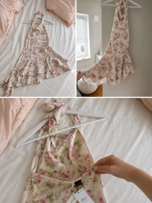Blommig volangklänning från Gina  - Supersöt kortklänning från Gina med blommigt mönster i rosa och grönt på vit botten. Klänningen har halterneck med knyt i nacken, volangdetaljer och omlottkänsla nedtill. Perfekt för sommarens alla tillfällen! Den är aldrig använd då jag hittade en bättre klänning till midsommar som den var tänkt till! 