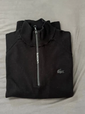 Svart ziptröja från Lacoste - Snygg svart ziptröja från Lacoste med halv dragkedja och ståkrage. Tröjan har diskret Lacoste-logga på bröstet och är i regular fit. Perfekt för en clean och stilren look, lätt att matcha med det mesta. FÖR MER INFO -> DM