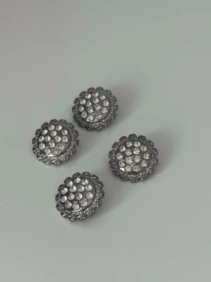 Knappar  - Fyra runda knappar i silverfärgad metall med strass på ovansidan, alla sitter kvar. 3cm 