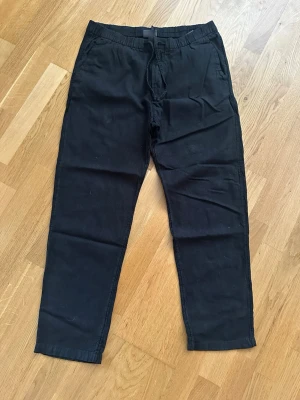 Svarta linnebyxor från H&M - Svarta linnebyxor från H&M med avslappnad passform och elastisk midja med dragsko. Byxorna har raka ben och sidofickor, vilket gör dem både snygga och bekväma. Materialet är lätt och luftigt linne, perfekt för dig som gillar stilrena och enkla plagg.