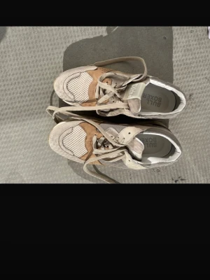 Beige och vita sneakers från Bullboxer - Snygga sneakers från Bullboxer i beige, vitt och brunt. Ovandelen är i mesh och mocka med coola paneler och detaljer. Skorna har beiga snören. Perfekta för dig som gillar streetstyle och vill ha något unikt.