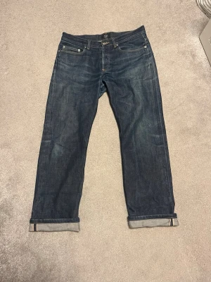 Mörkblå jeans från A.P.C. - Säljer ett par mörkblå jeans från A.P.C. i klassisk rak modell. Jeansen har fem fickor, uppvikta benslut och är tillverkade i kraftig denim. Perfekta för dig som gillar stilrena och tidlösa jeans.