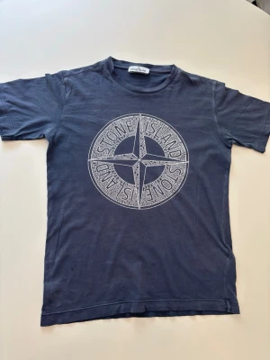 Mörkblå Stone Island t-shirt  - Snygg blå t-shirt från Stone Island med stort vitt logotryck på bröstet. Jättebra skick och i princip aldrig använd då den varit för liten. Inga defekter eller så och passar till mycket, en väldig snygg sommar T-shirt. Kontakta mig för mer, pris kan diskuteras som vanligt!😇