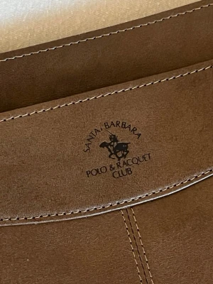 Datorväska Polo - Brun datorväska i konstläder från Santa Barbara Polo & Racquet Club. Perfekt för att bära din dator på ett snyggt och trendigt sätt.
